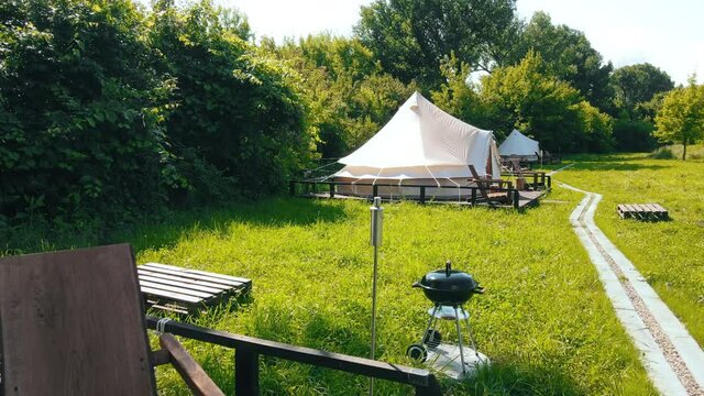 Glamping tents with chairs in the nature, green grass and trees, trail
