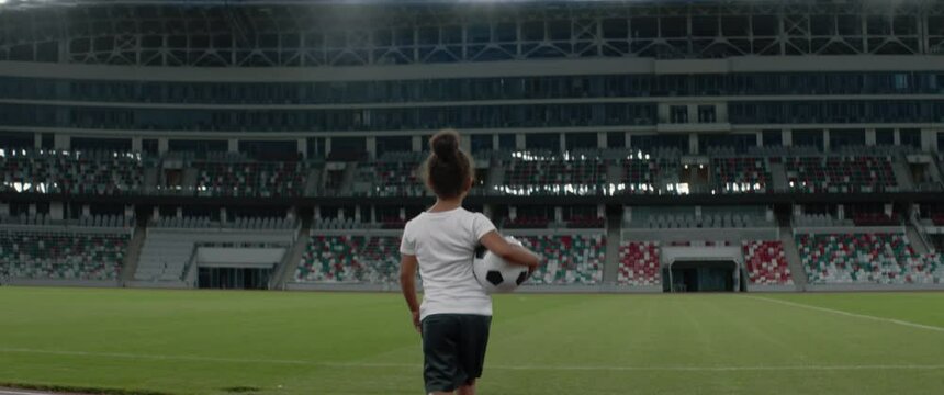 Portrait of African American Black dreamer child girl walking onto the field of huge soccer football stadium, holding a ball, dreaming of becoming professional player, soccer star. Women sport concept
