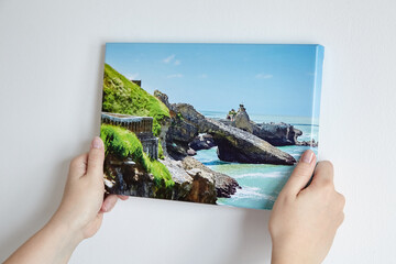 Canvas print with gallery wrap. Woman hangs photography on white wall. Hands holding photo canvas...