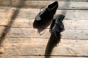 Professional black ballroom dance shoes lie on the wooden floor.