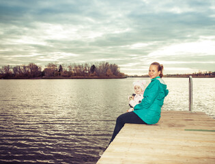 mom and daughter are sitting on the pier at sunset