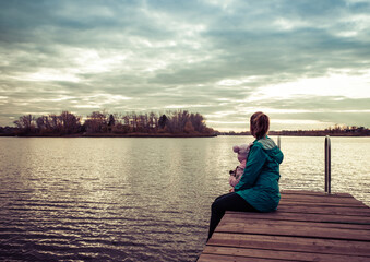 mom and daughter are sitting on the pier at sunset