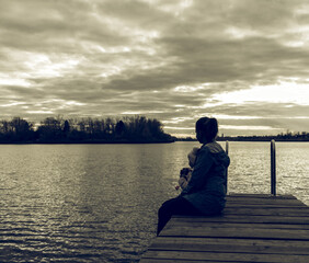 mom and daughter are sitting on the pier at sunset