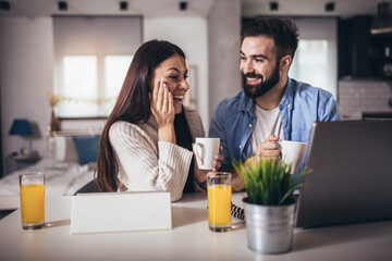 Young couple using a laptop and digital tablet together working at home