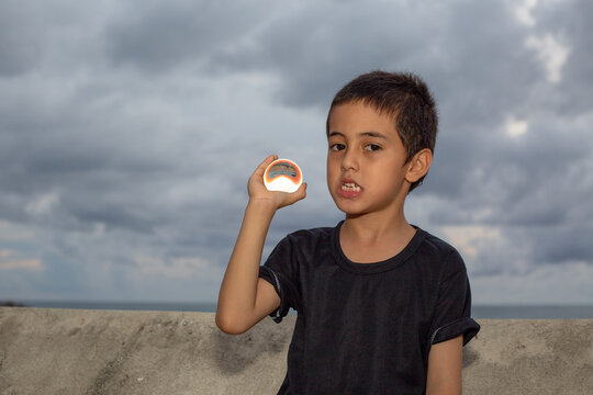 .A boy holding a crystal ball beside wave barrier at Kata beach Phuket Thailand..cloud above island in sunset background..smiling face of happy boy relax concept..