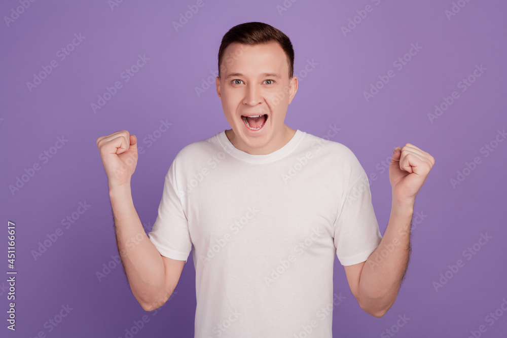 Wall mural Portrait of astonished mad man raise fists scream on violet background