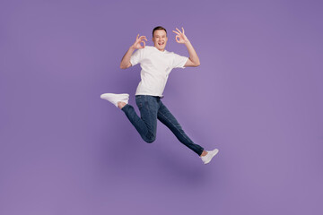 Portrait of crazy promoter guy jump run hands show okey on purple background