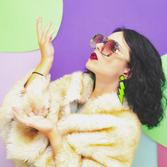 A pretty lady with sunglasses, dark red lipstick, a white faux fur coat and earrings on a pop art background
