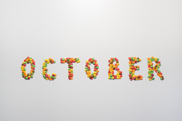October inscription on a white background. Confectionery sprinkles in the form of multi-colored maple leaves