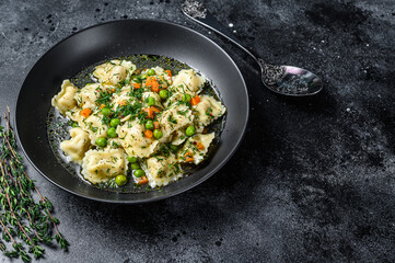 Dumplings Soup with Ravioli pasta in a bowl with greens. Black background. Top view. Copy space