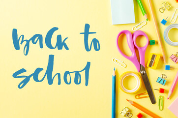 Back to school. Handwritten inscription. School supplies on a yellow paper background.