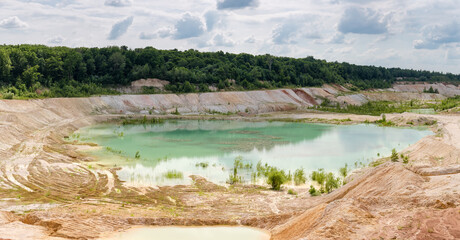 Small shallow turquoise quarry lake in abandoned kaolin pit, panorama