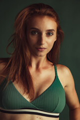 Close-up portrait of young beautiful red-headed woman without makeup isolated over dark green...