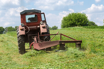 Rotary mower on small old tractor during operation on hayfield