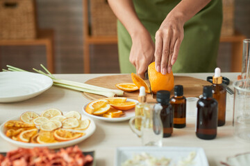 Close-up image of woman in apron cutting orange wehn prepearing thin slices for making oragnic soap