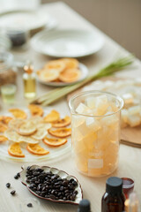 Jar with cubes of soap base, small plate with coffee beans and dry orange slices on table in workshop
