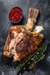 Roasted pork knuckle eisbein on a wooden board with herbs. Black background. Top view