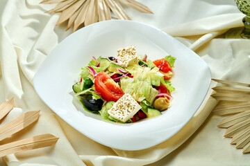 Greek salad with tomatoes, olives and feta cheese in a white plate on a tablecloth