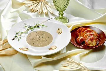 Mushroom cream soup with a bun in a white plate on a tablecloth