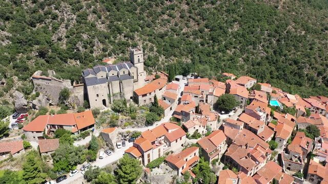 General summer view of picturesque French village of Eus in natural region of Conflent with tightly grouped houses, medieval church and castle ruins on top of hill