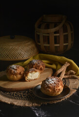 luxury home made chilled vanilla cream puff pastry choux with sugar powder on wood plate and cloth in black background and bamboo basket prop dessert halal menu