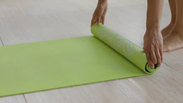 Woman rolls upa rug of yoga in yoga class room, yoga time end, yoga class.