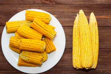 Sweet yellow corn, boiled and raw, lies on a wooden table.