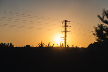 High voltage tower to conduct electricity in a sunset landscape with yellowish sun
