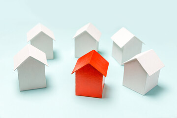 Obraz premium Simply design with miniature red toy model house in among white houses isolated on pastel blue background. Real estate property industry. Community unique neighborhood choice concept.