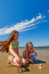 Fototapeta premium Children build a sand castle on the coast. Against the backdrop of blue sky and sunny summer water.