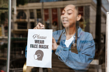 Black waitress sticking announce poster while working in cafe