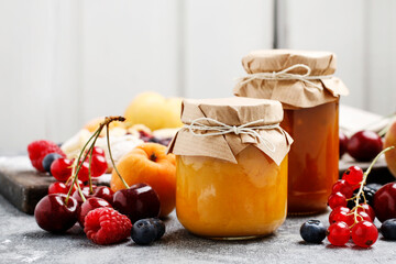 Two jars with peach jam and fresh fruits on wooden table.