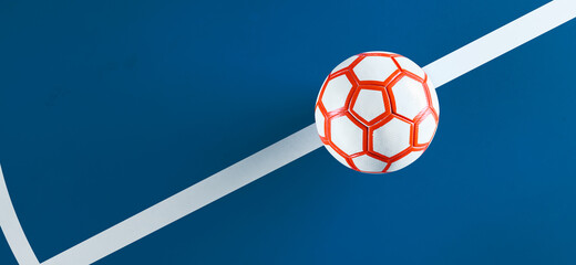 Close-up of a white futsal ball with orange hexagon stripes on the line of a blue indoor soccer...