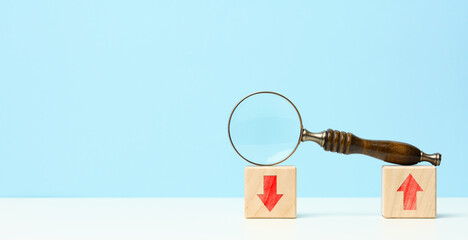 wooden magnifier on wooden cubes with up and down arrows. Market fluctuations concept, currency...