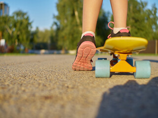 Girl kid standing on the asphalt road and yellow penny board with blue wheels on street background during sunset time.