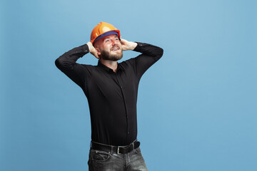 Portrait of funny bearded man, builder, designer or architect with professional equipment isolated on blue studio background.