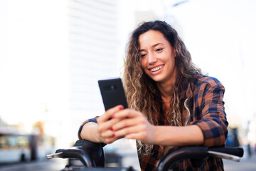 Beautiful smiling girl on electric bicycle on the street. Beautiful girl using the phone.