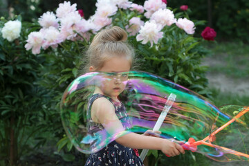 Girl playing with soap bubbles on a background of flowers