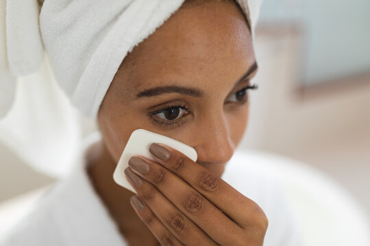 Mixed race woman in bathroom cleansing her face with cotton pad for skin care