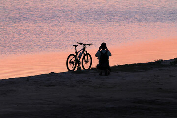 Man beside the bike takes a picture of the sunset near the water