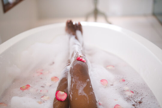 Low section of african american woman relaxing in pampering foam bath with rose petals
