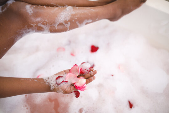 Close up of african american woman having pampering foam bath, adding rose petals