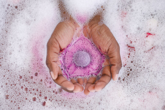 Close up of hands of african american woman having pampering bath, holding fizzing bath bomb