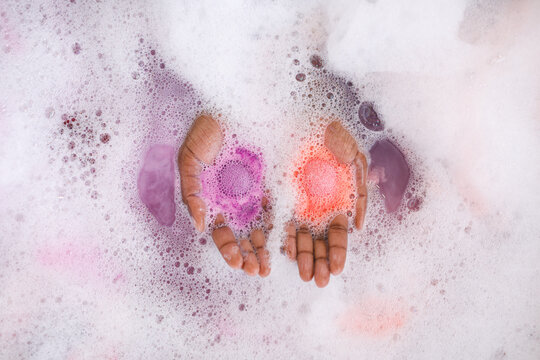 Close up of hands of african american woman having pampering bath, holding fizzing bath bombs