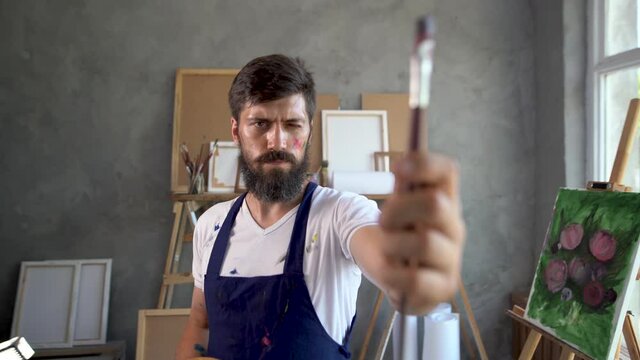 a male artist is in his own studio and measures the proportions with a paint brush.