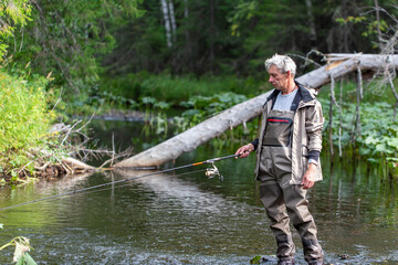 Portrait of fisherman in waders with spinning rod on the river. Spinning fishing - obrazy, fototapety, plakaty