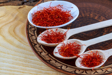 Saffron stamens in wooden spoons on a porcelain plate. Stand on a wooden background.