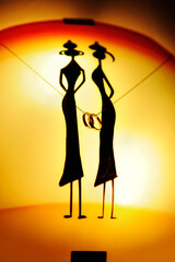 Two gold rings on the turned on wall lamp with a yellow light depicting the silhouettes of two girls.
