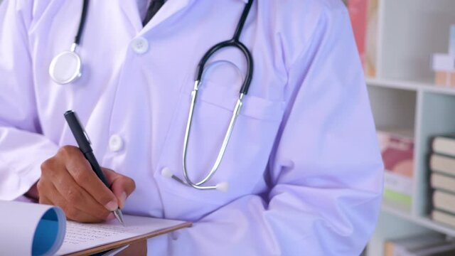 Doctor in uniform writing a short note and making doctor order after examining in clinic. 4K