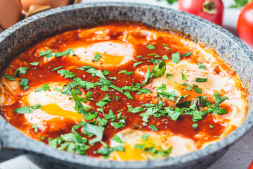 Traditional Israeli shakshuka in gray frying pan. Fried eggs in tomato sauce, close-up.